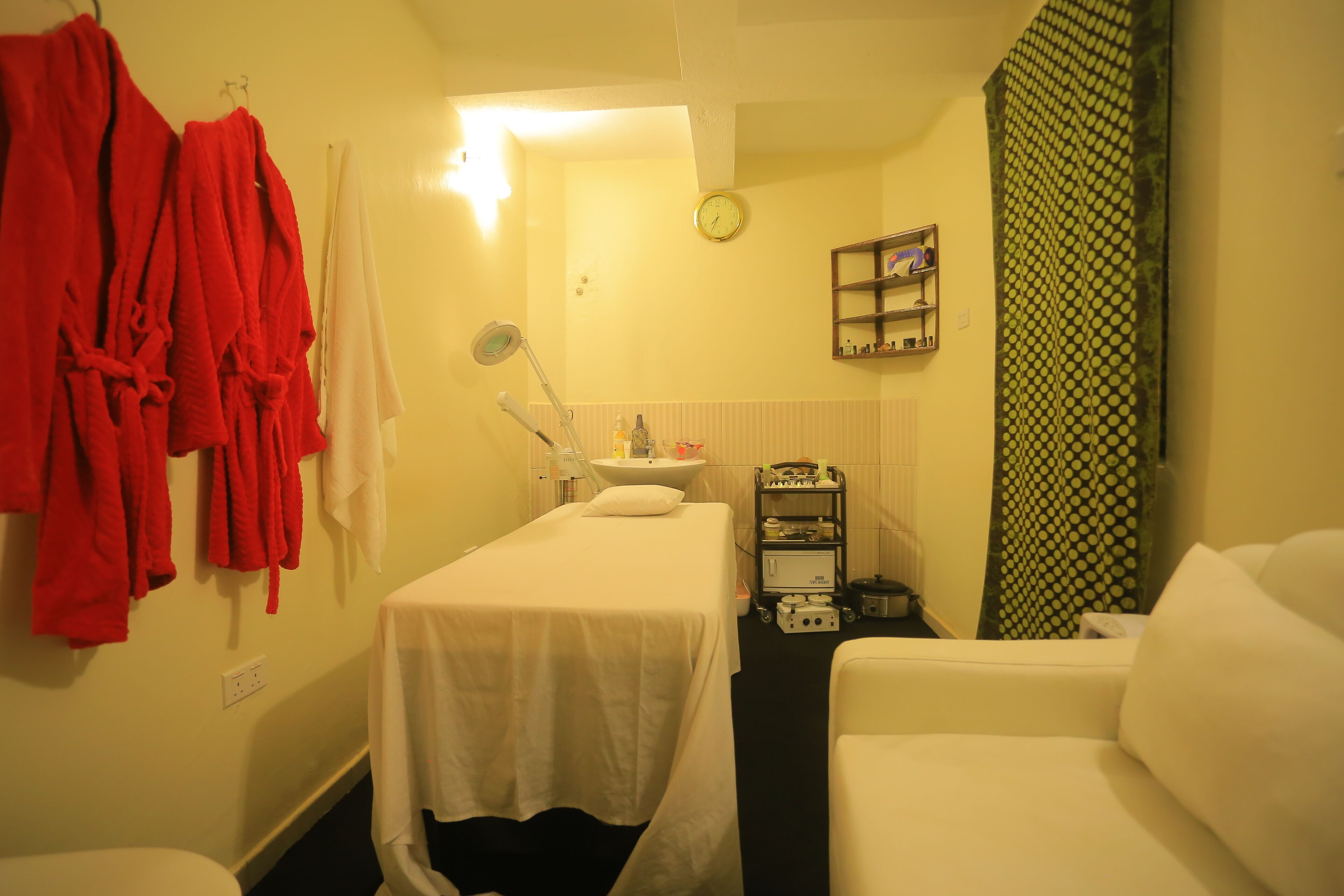 A room with a bed, a small table with a mirror, a sink, and a shelf with toiletries.