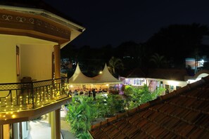 An outdoor dining area with tables and chairs, surrounded by lush greenery and a covered seating area with a thatched roof. - Mowicribs Hotel & Spa (Entebbe)