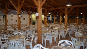 A spacious indoor dining area with numerous white plastic chairs and tables, wooden beams on the ceiling, and hanging plants. - Villaggio Riccio (Mattinata)