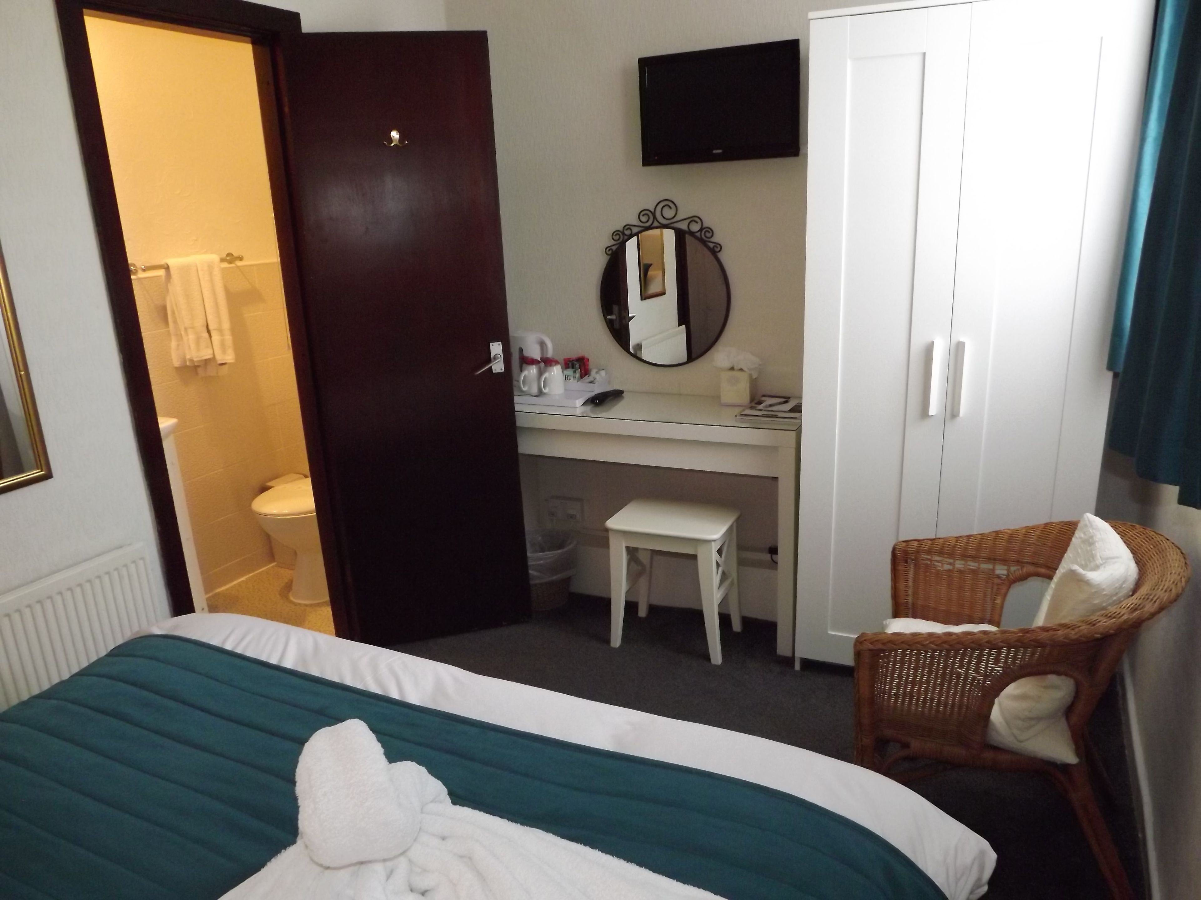A hotel room with a bed, a desk, a chair, a wardrobe, a mirror, and a television.