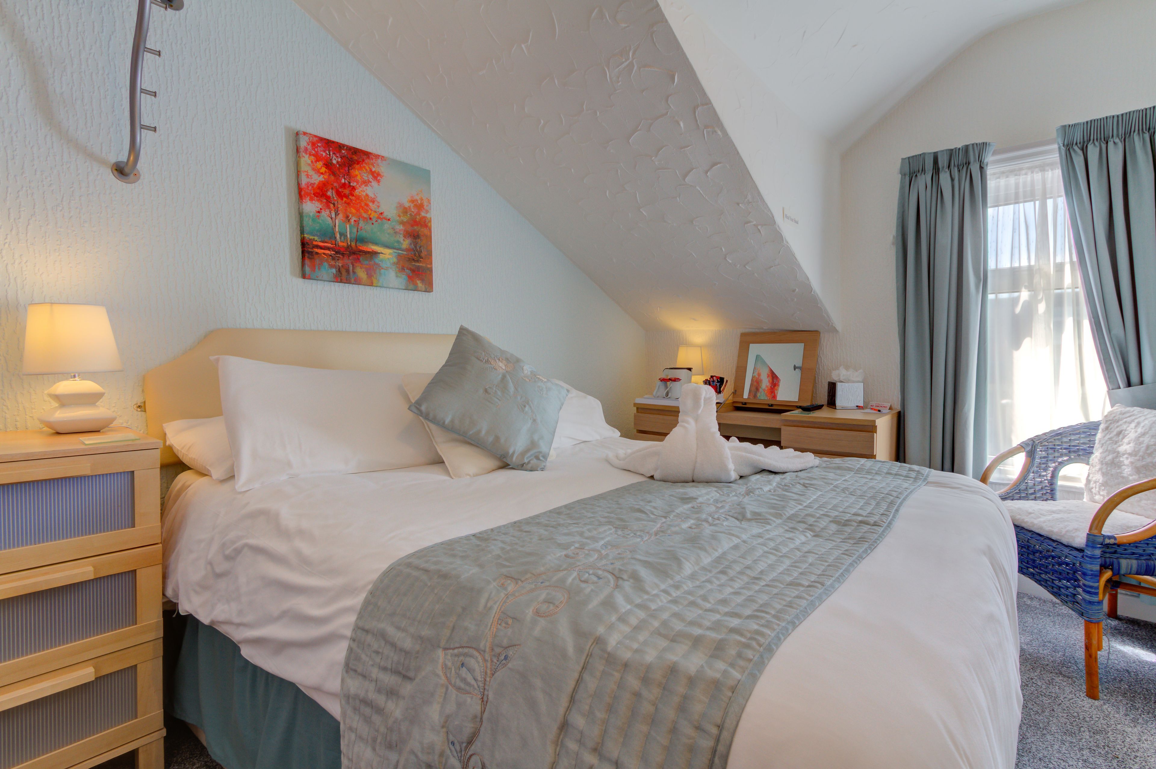 A hotel room with a large bed, a bedside table with a lamp, a chair, and a painting on the wall.