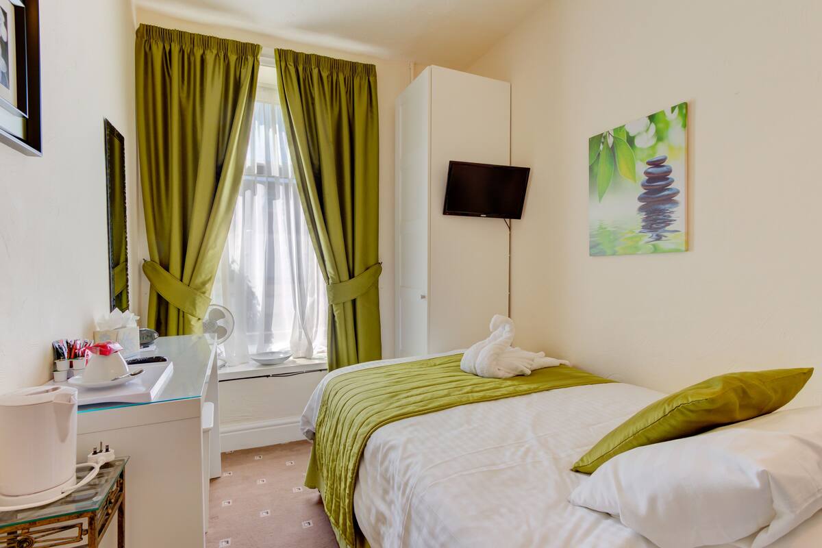 Quarto de hotel com cama, escrivaninha com ventoinha, televisão na parede e um quadro.