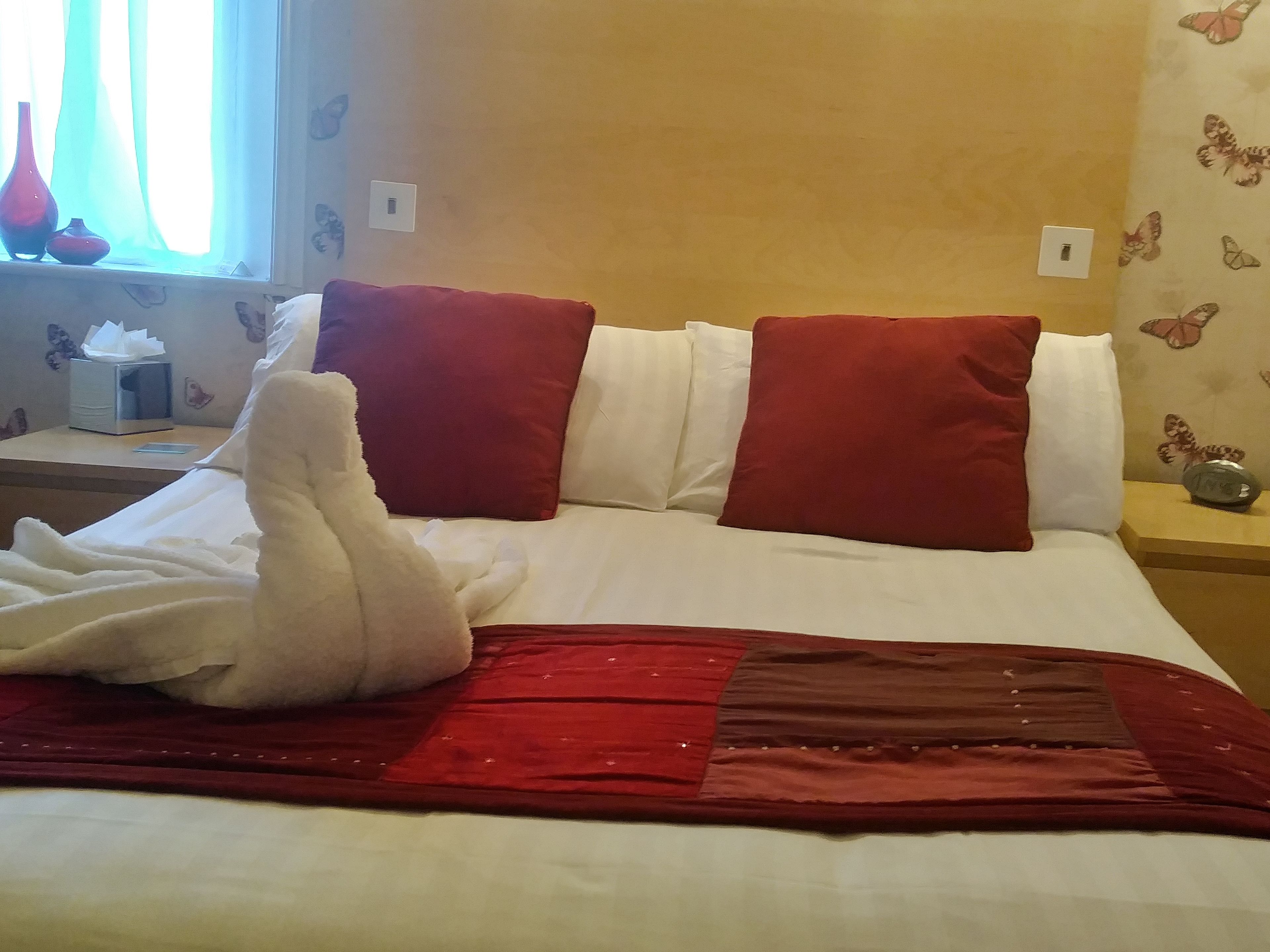 A neatly made bed with a red and white bedspread, two red pillows, and a white towel.