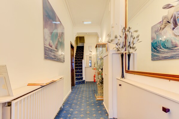 A hallway with a blue carpet, white walls, and a staircase leading to an upper floor.