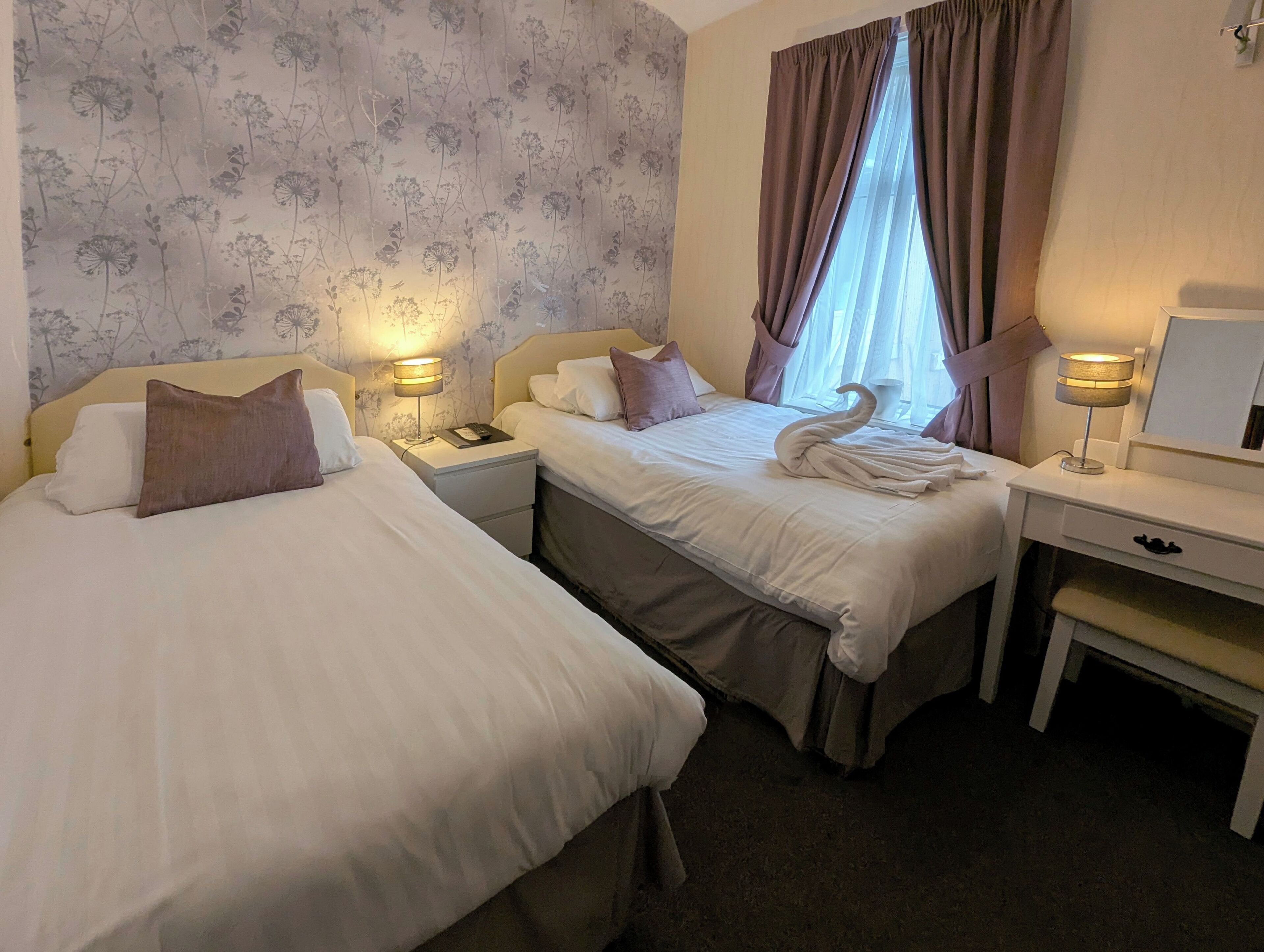 A hotel room with two beds, a desk, and a nightstand with lamps.