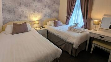 A hotel room with two beds, a desk, and a nightstand with lamps.