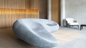 A modern interior with a unique ceiling design, a large stone sculpture, and a minimalist seating area.