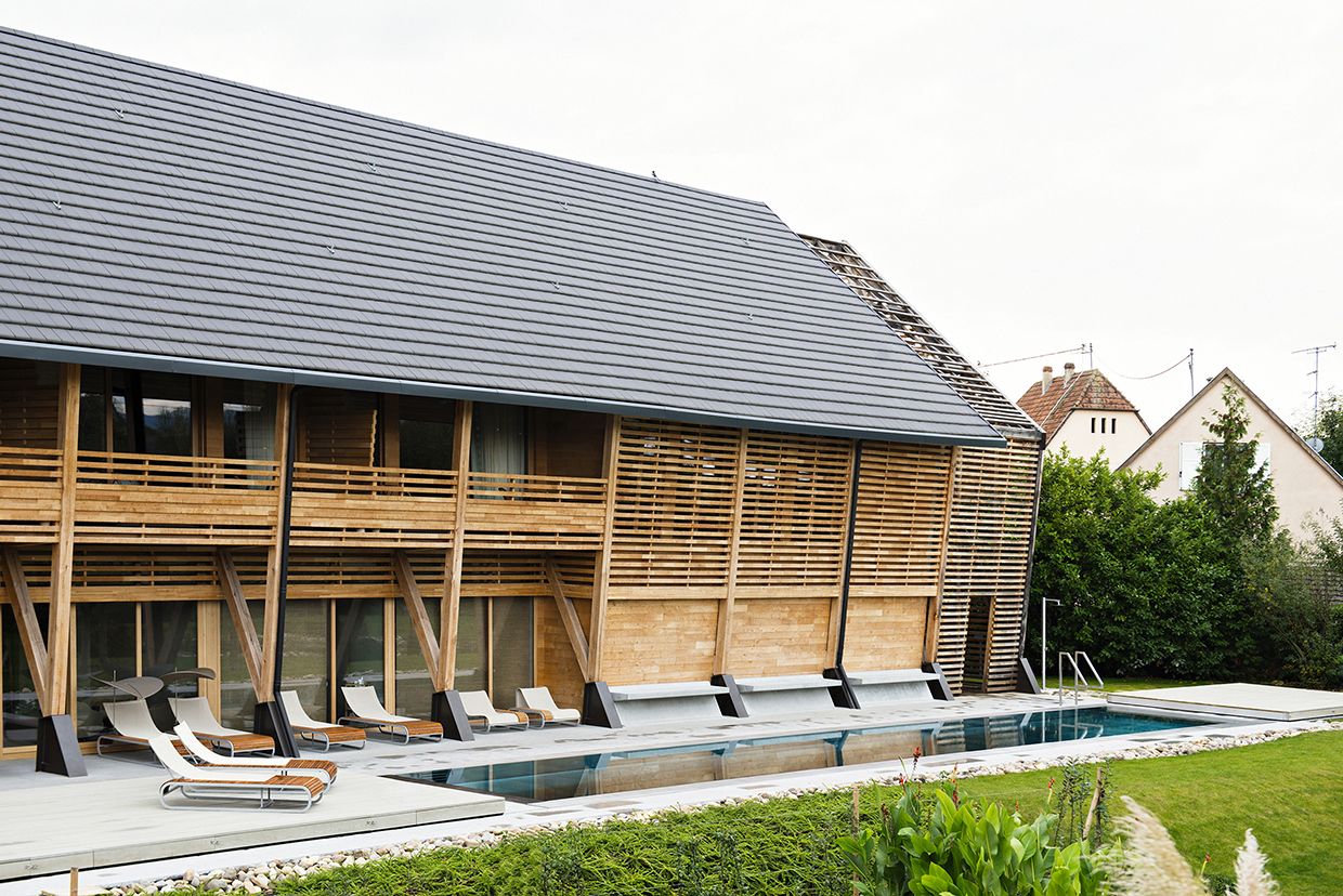 A modern building with a swimming pool, wooden slatted walls, and lounge chairs.