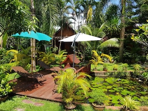 A tropical garden with a wooden deck, lounge chairs, and umbrellas. - Thongbay Guesthouse Luang Prabang (Luang Prabang)