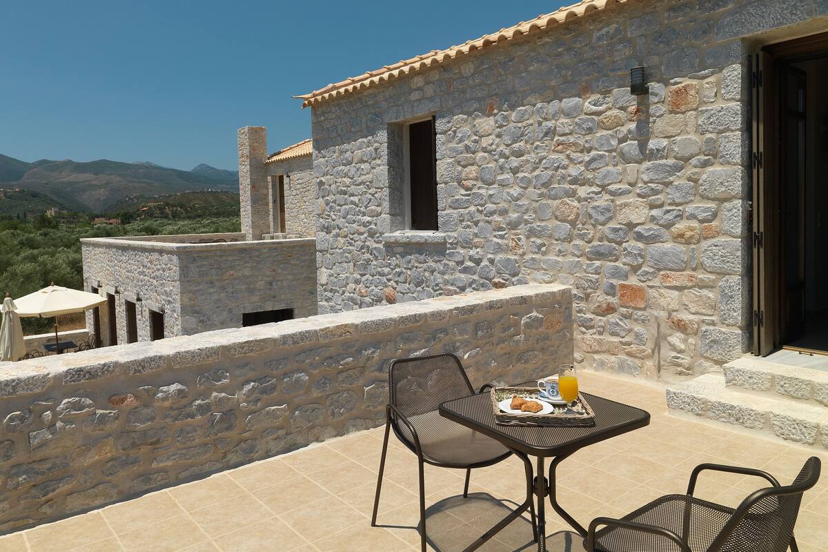 Un bâtiment en pierre doté d’une terrasse carrelée, d’un espace extérieur aménagé pour s’asseoir et offrant une vue sur le paysage.