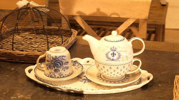 A tea set on a tray with a wicker basket and a chair in the background. - Kamares Villas (East Mani)
