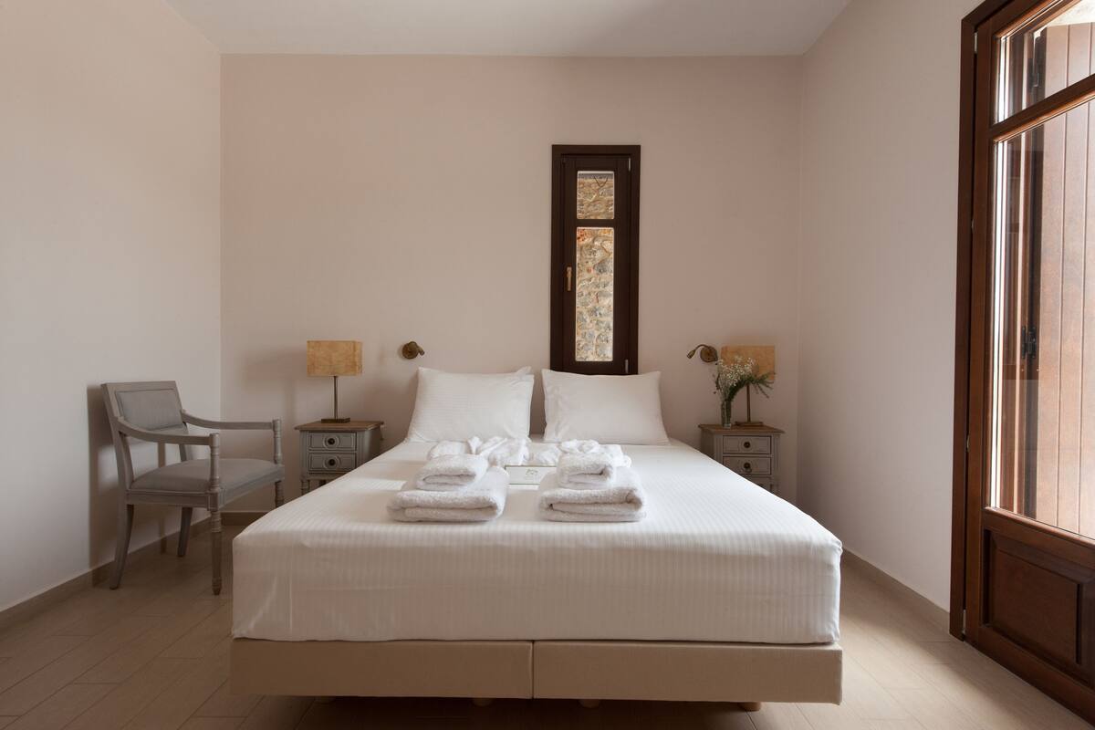 Un lit bien fait, avec des serviettes, une chaise et deux tables de chevet avec des lampes.