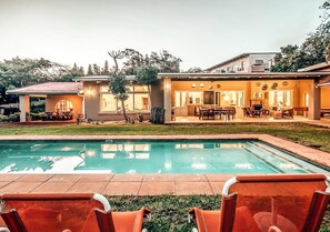 A residential property with a swimming pool, outdoor seating, and a well-maintained lawn. - Ngoye Lodge (eMthunzini)