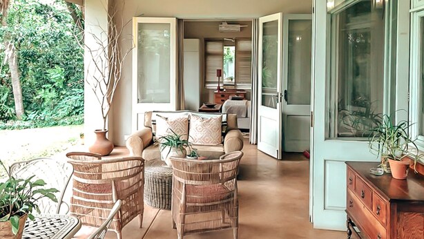 A spacious living area with wicker furniture, a dining table, and a view of the garden. - Ngoye Lodge (eMthunzini)