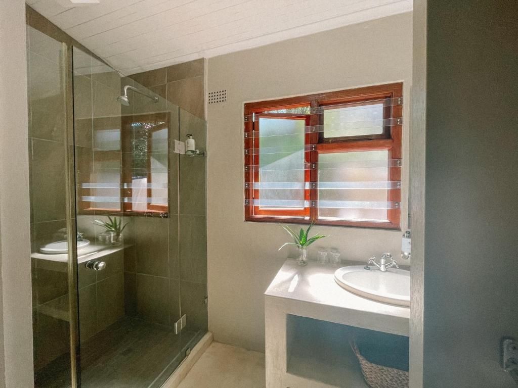 Une salle de bain avec une douche à parois de verre, un lavabo et une fenêtre avec des stores.