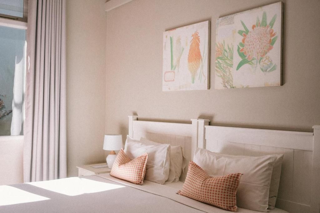Een slaapkamer met een bed, kussens, een nachtkastje, een lamp en wanddecoratie.