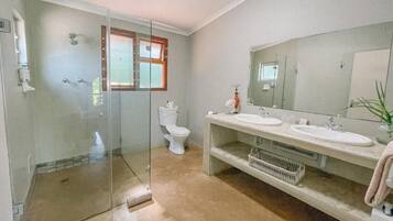 Un baño con cabina de ducha de vidrio, inodoro y tocador doble con espejo.