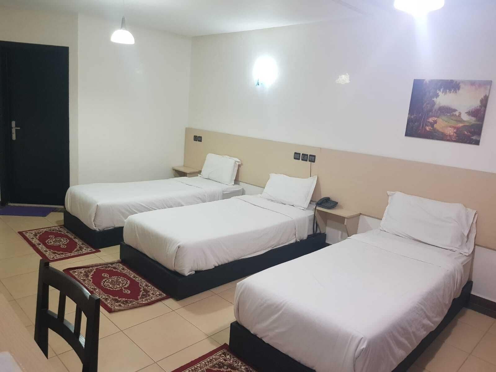 Quarto de hotel com duas camas de solteiro, uma pequena mesa de cabeceira com telefone, uma luminária na parede e uma porta.