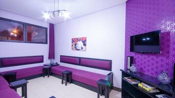 Una habitación con una decoración en morado y blanco, que incluye un sofá, un televisor y una estantería.