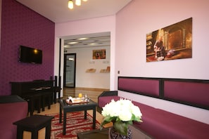 A lobby with a seating area, a television mounted on the wall, and a painting.