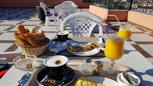 Un desayuno con pan, un plato de comida, una taza de café, un vaso de jugo de naranja y condimentos sobre una mesa.
