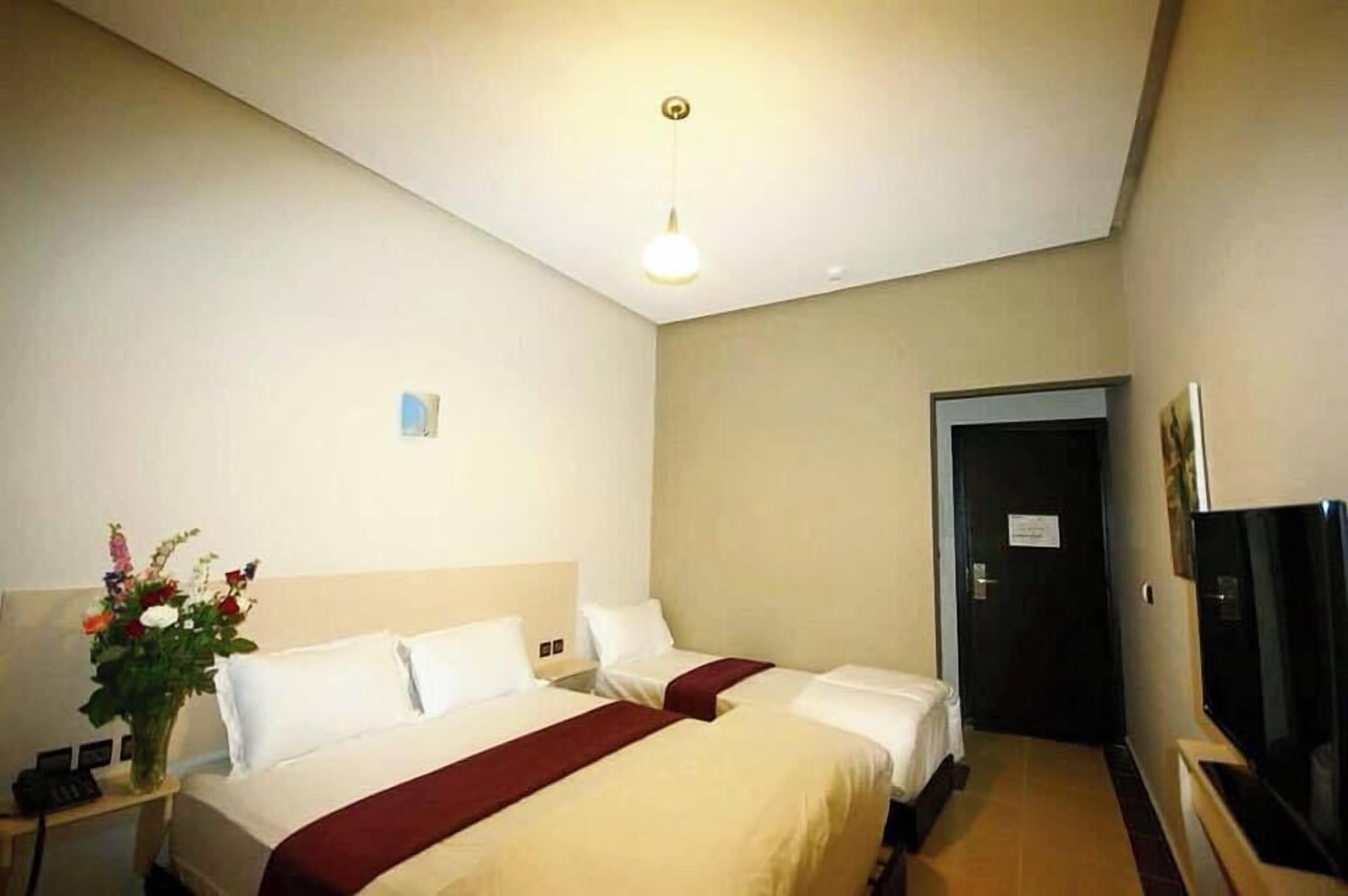 Une chambre d’hôtel avec deux lits, une table de chevet avec un téléphone, un vase de fleurs et un téléviseur.