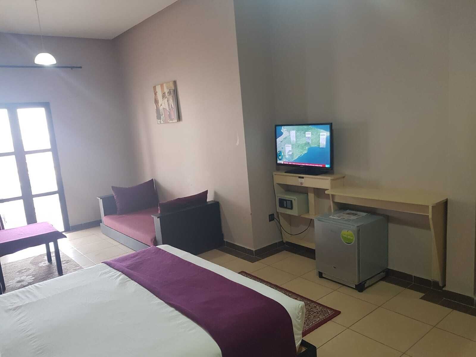 A hotel room with a bed, a desk, a television, and a small refrigerator.