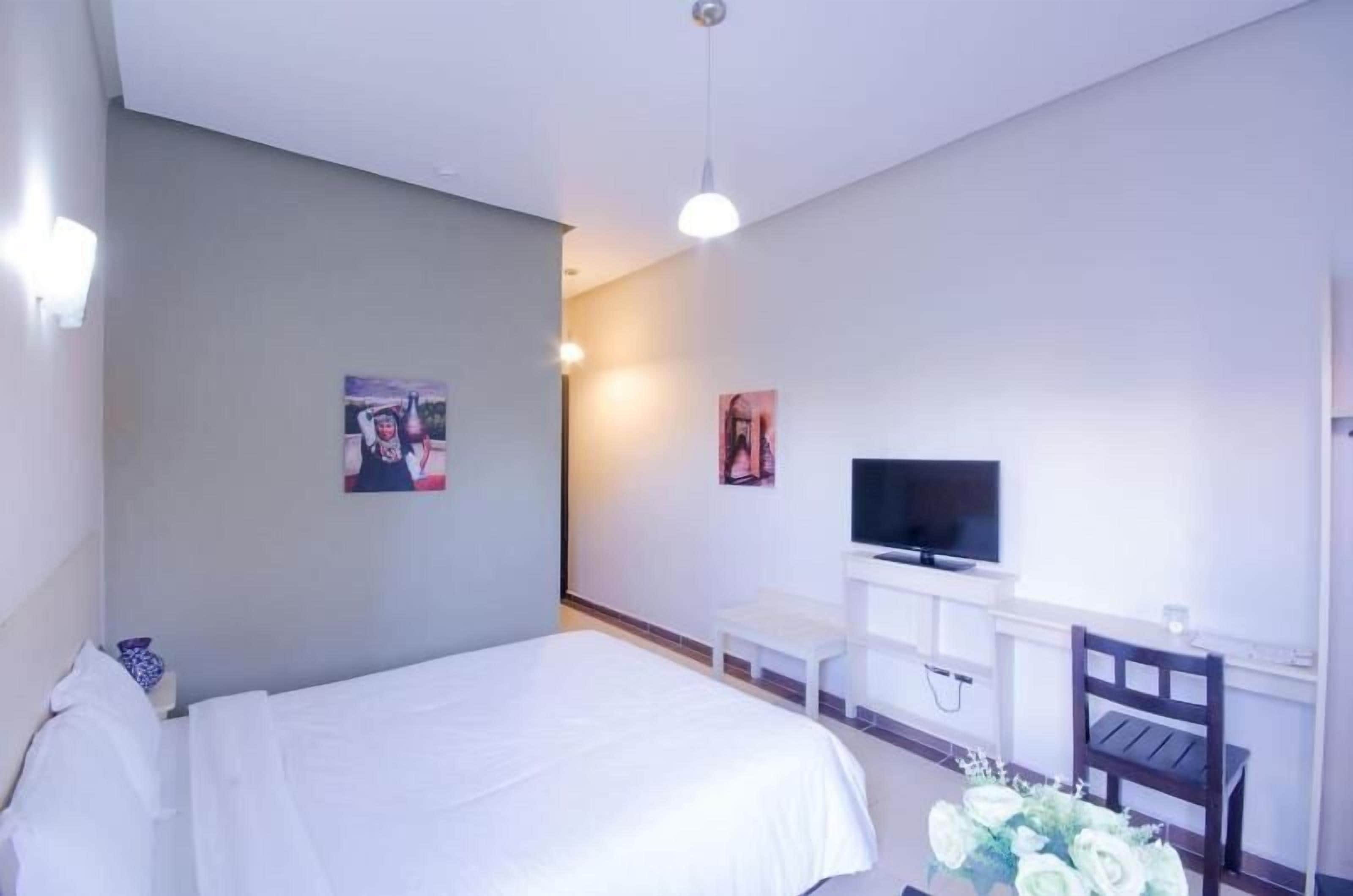 A hotel room with a bed, a desk, a chair, a TV, and wall art.