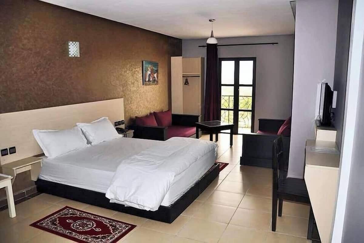 A hotel room with a large bed, a desk, a chair, a TV, and a window with curtains.