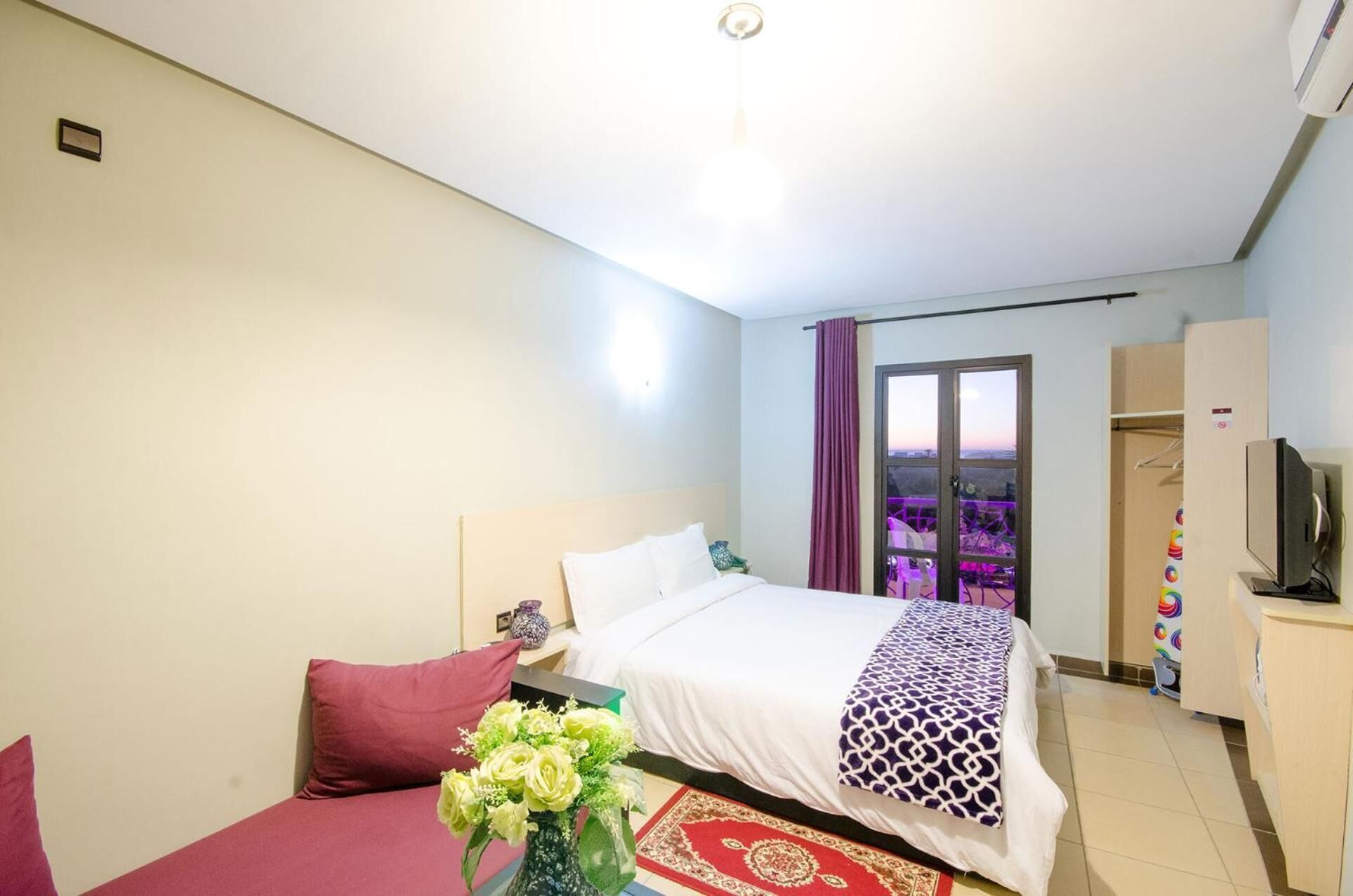 A hotel room with a bed, a desk, a chair, a TV, and a window with a view.
