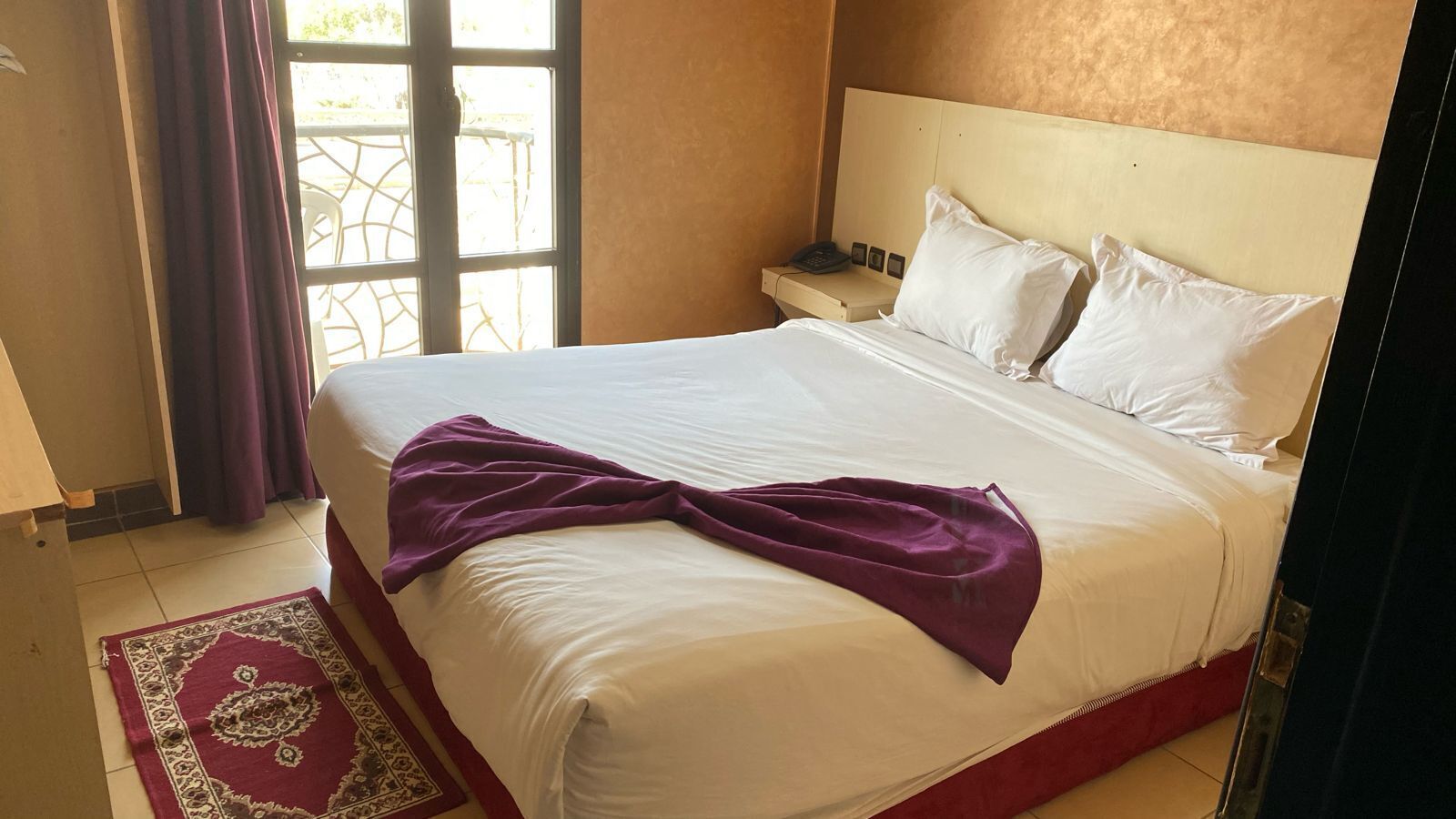 Una habitación de hotel con cama, mesita de noche, teléfono y ventana con cortinas.