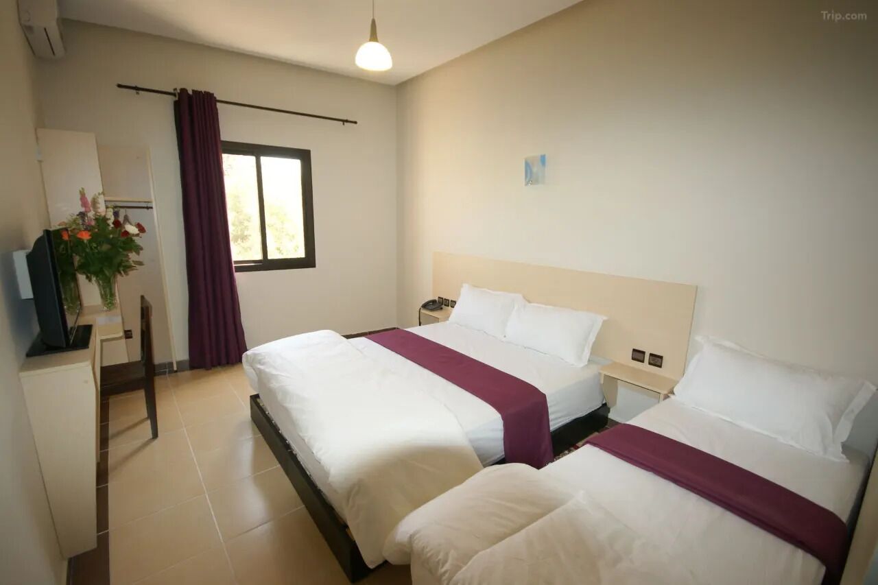 Ett hotellrum med två sängar, ett skrivbord, en stol, en TV och ett fönster med gardiner.