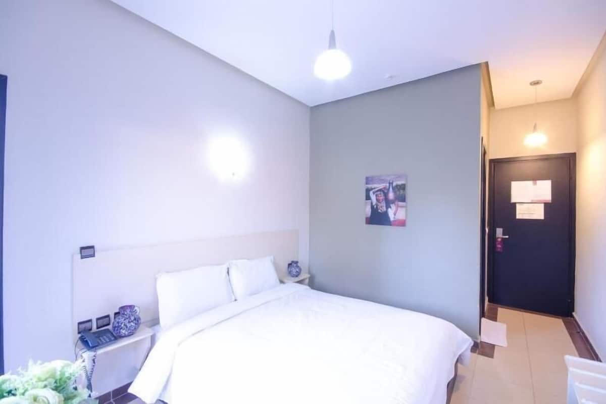 A hotel room with a bed, bedside table, lamp, and a door with a sign.