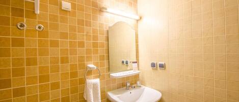 A bathroom with yellow tiles, a white sink, a towel rack, a mirror, and a paper towel dispenser.
