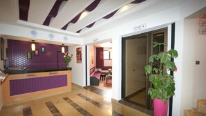 Zona de recepción de un hotel, con mostrador de recepción, un reloj y una planta en maceta.