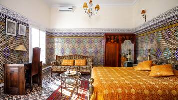 Una habitación con suelo estampado, un sofá con cojines, una cama con cubrecama estampado, un mueble de madera y una araña.