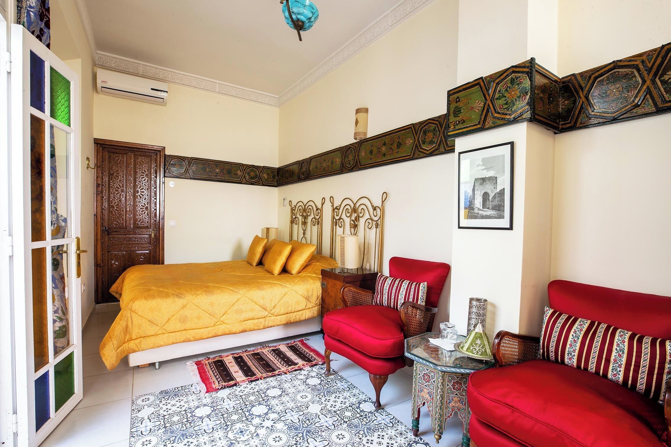 Un dormitorio con cama, un sillón rojo, sofá, alfombra estampada y un borde decorativo en la pared.