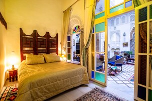 Ein geräumiges Schlafzimmer mit einem großen Bett, einem Holzkopfstück und Blick auf den Innenhof durch eine offene Tür.