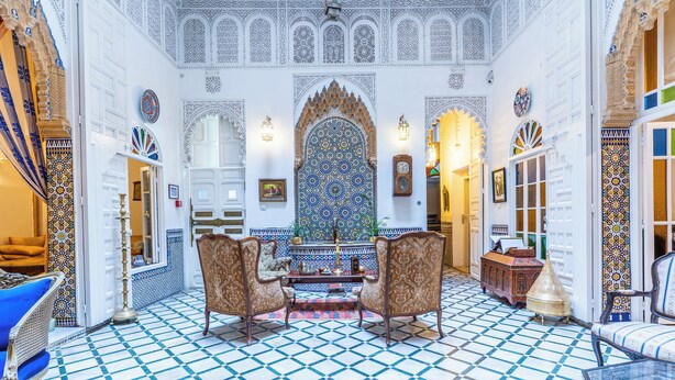 Una habitación con suelo de baldosas estampadas, paredes blancas ornamentadas y un arco decorativo central.