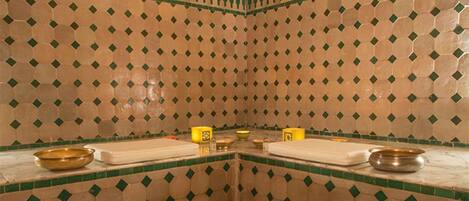 Un baño con pared de azulejos con un diseño geométrico y una zona de lavamanos central con dos lavabos y un espejo.