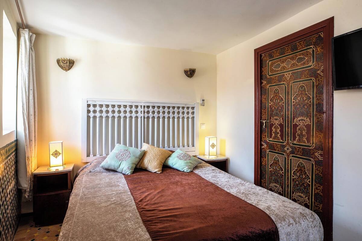 Een slaapkamer met een bed, twee nachtkastjes met lampen, een decoratieve deur en een radiator.