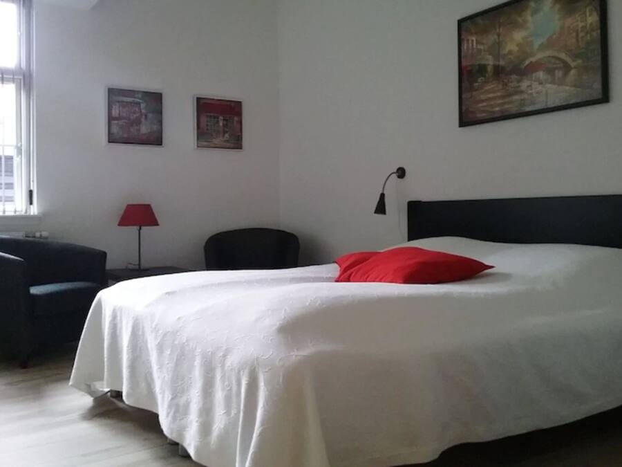 A hotel room with a large bed, a desk, a chair, and two paintings on the wall.