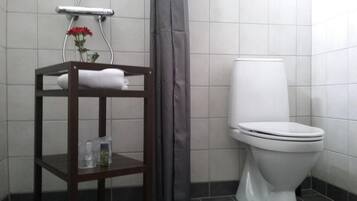 Un baño con inodoro blanco, un estante de madera con una toalla y un cabezal de ducha.
