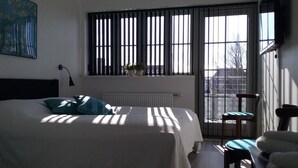 A bedroom with a bed, a window with blinds, a radiator, a chair, and a painting on the wall. - Hals Hotel (Hals)