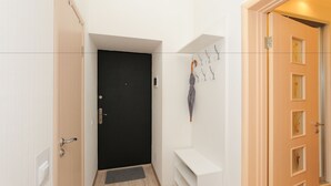 Un pasillo con una puerta negra, un banco blanco y un perchero con un paraguas gris.