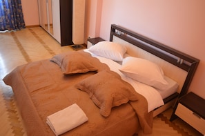 A neatly made bed with a brown blanket and pillows, a bedside table with a lamp, and a mirror on the wall.