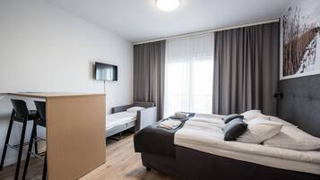 A modern hotel room with a bed, a desk, two chairs, a flat-screen TV, and a large window with curtains.