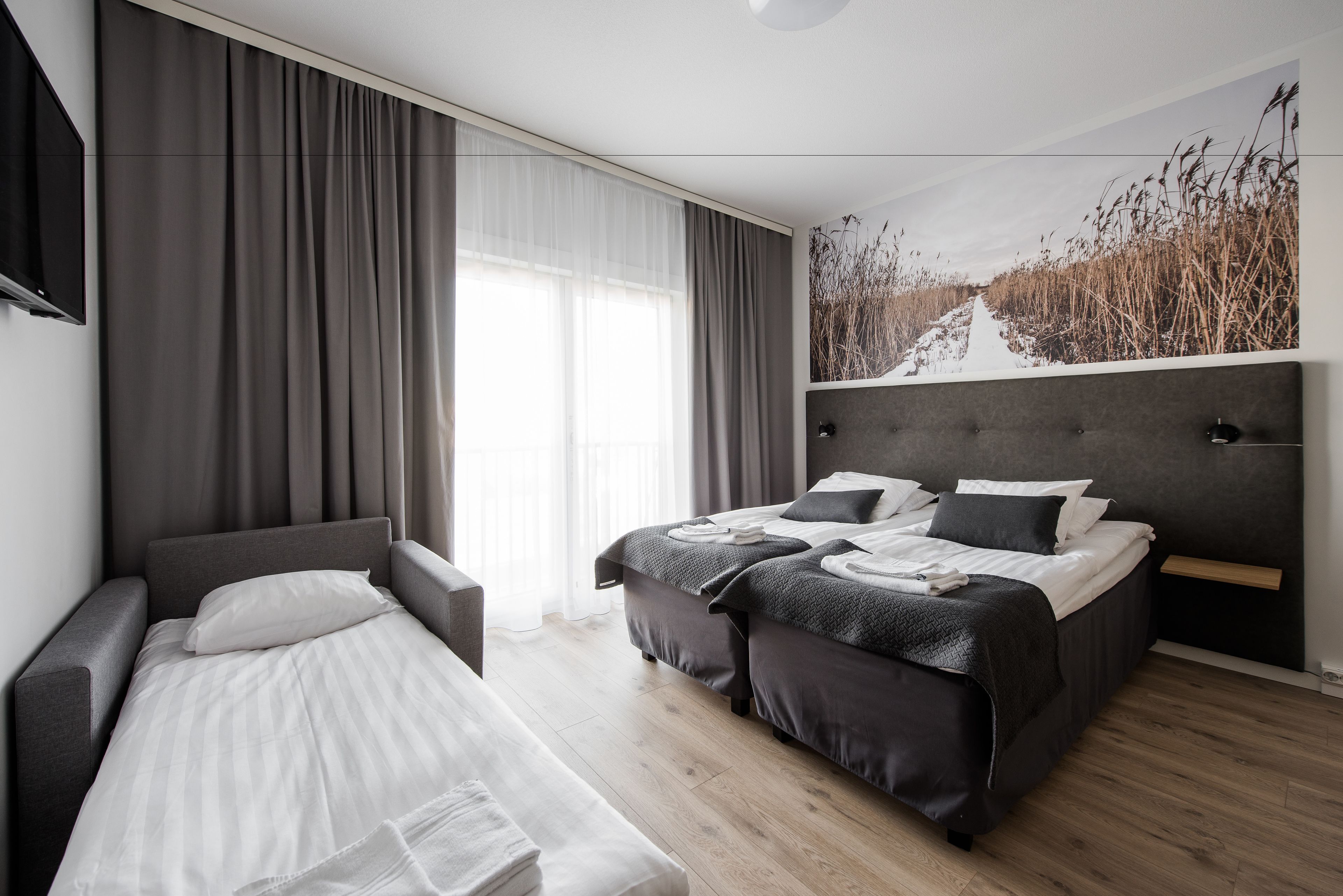 Una habitación de hotel moderna con una cama grande, otra más pequeña, un sofá y un televisor.