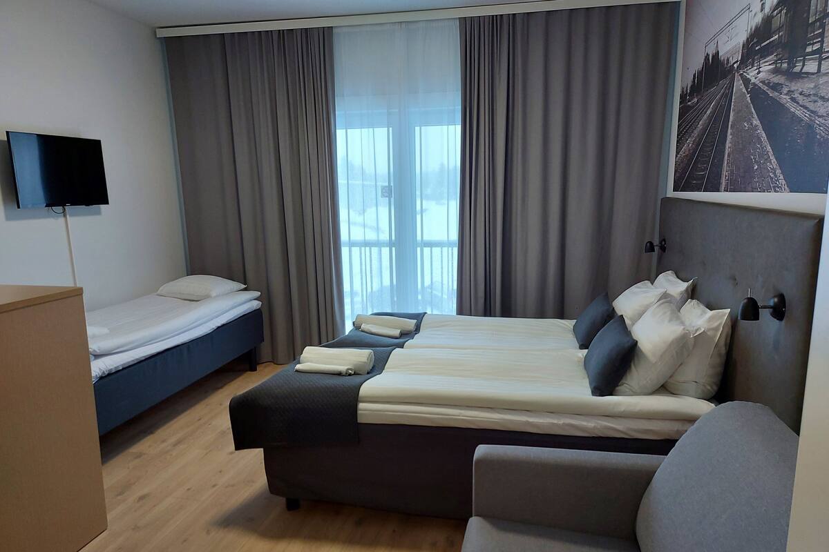 A hotel room with a large bed, a smaller bed, a desk, a chair, and a TV.