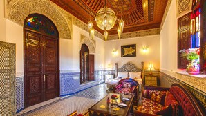 A traditional Moroccan interior with ornate wooden doors, a patterned tiled floor, a chandelier, and a sofa set. - Riad Fes Maya (Fes)